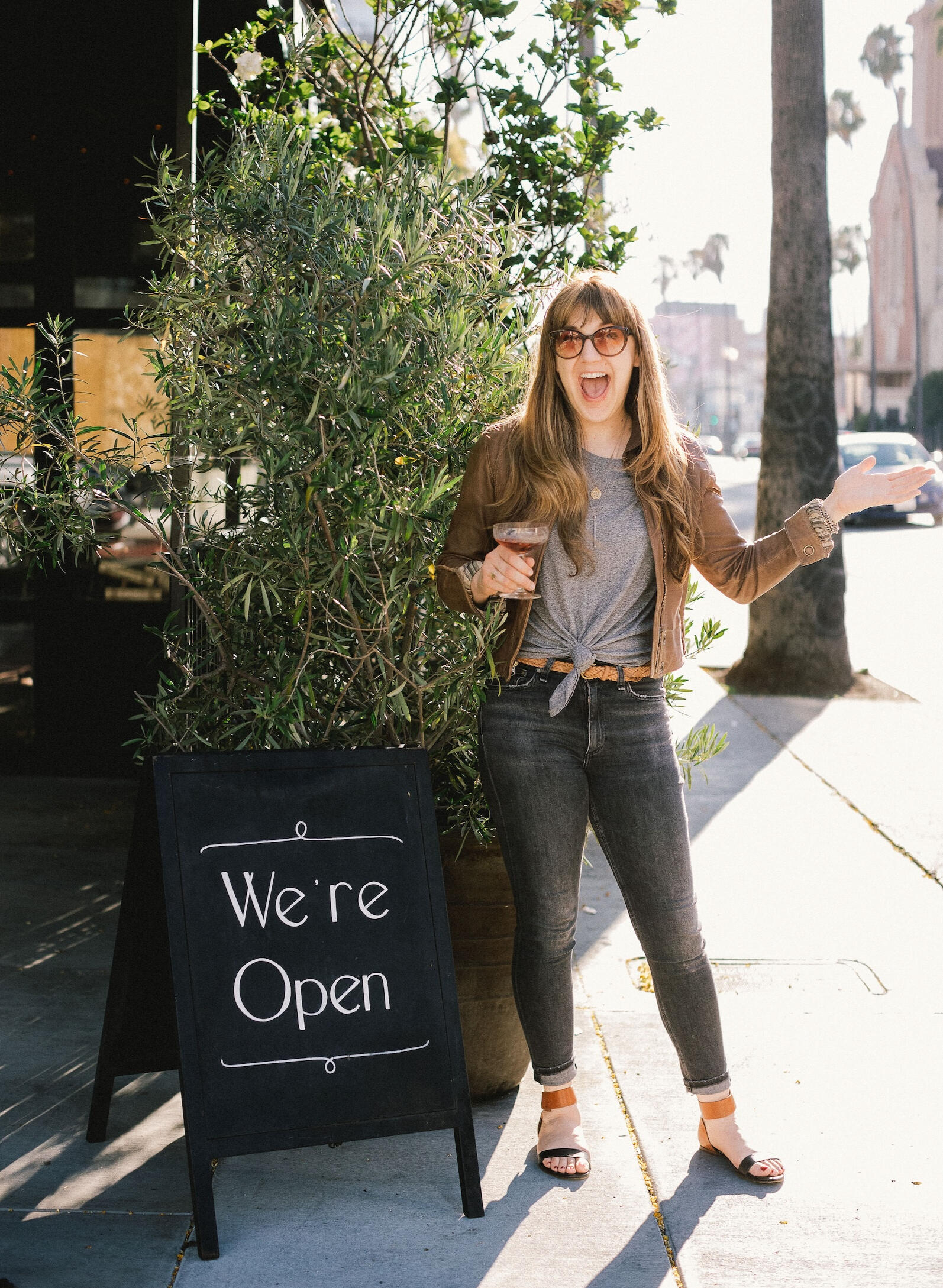 Open for business A woman wearing sunglasses and a leather jacket is standing on a Hollywood street holding a coupe of rosé Champagne